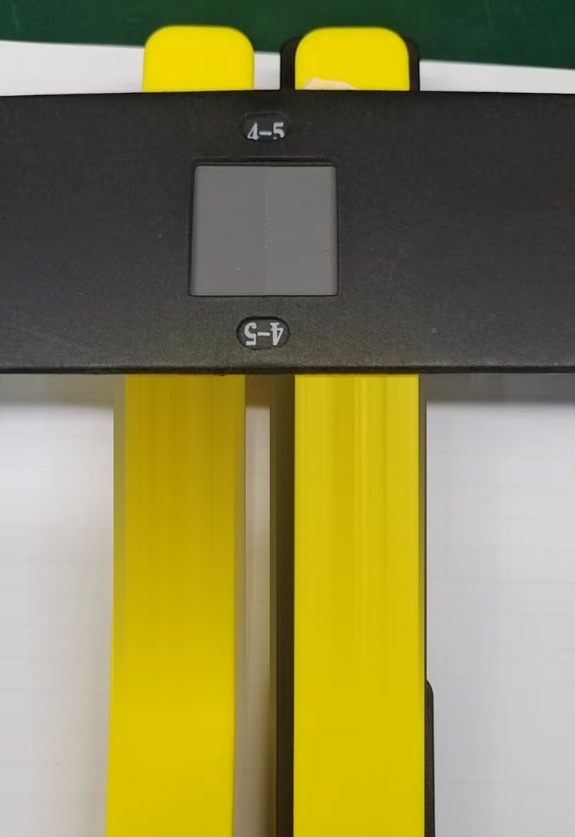 A grey scale card held across two yellow trolley tubes on a white surface, with the grade 4-5 reference pair visible in the card window