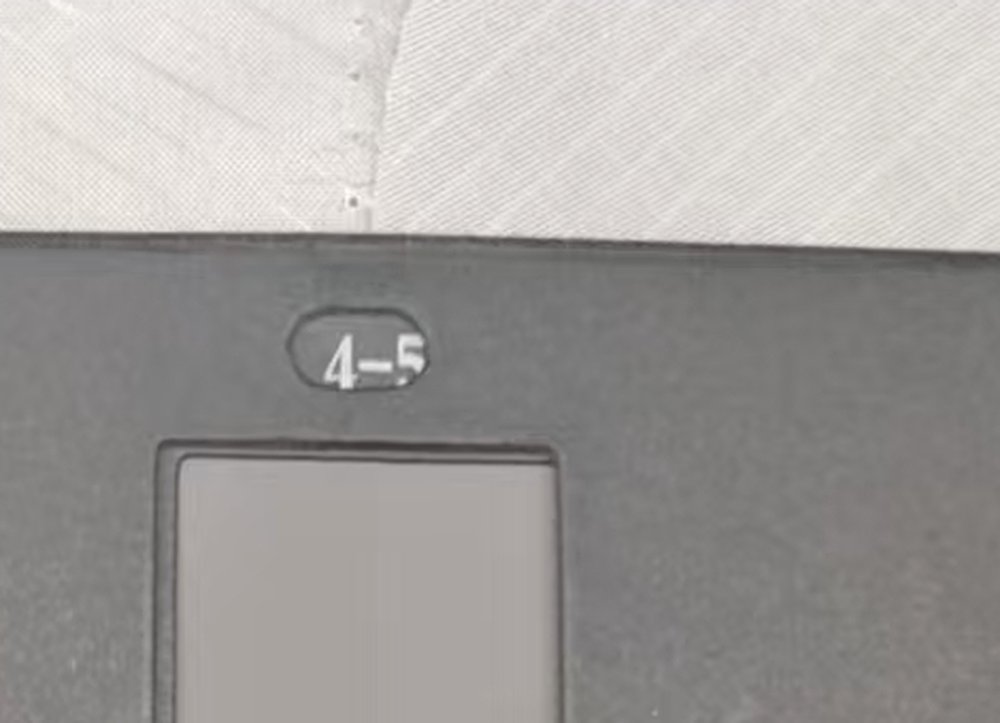 Close view of a grey scale reference card marked 4-5 above its open viewing window, resting against white woven fabric